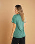 Woman wearing a green t-shirt and black pants against a beige background