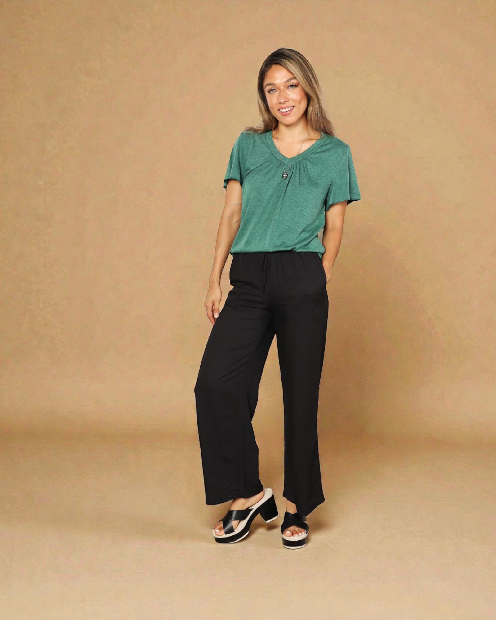 Woman wearing a green top and black pants against a beige background