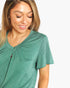 A woman wearing a green short-sleeve V-neck top with a gathered neckline, shown against a plain light background.