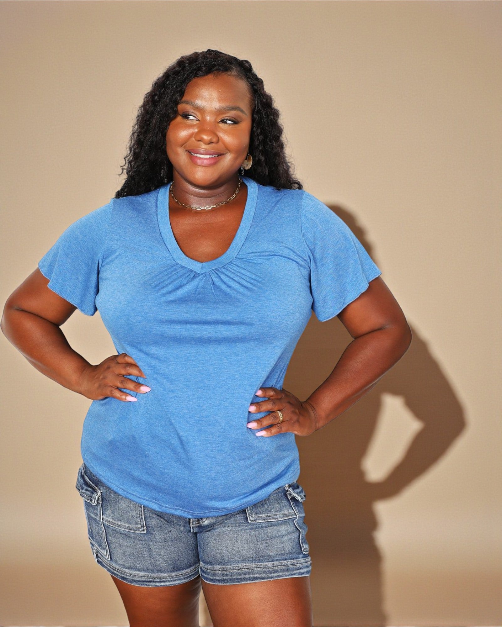 Woman wearing a blue t-shirt and denim shorts against a beige background