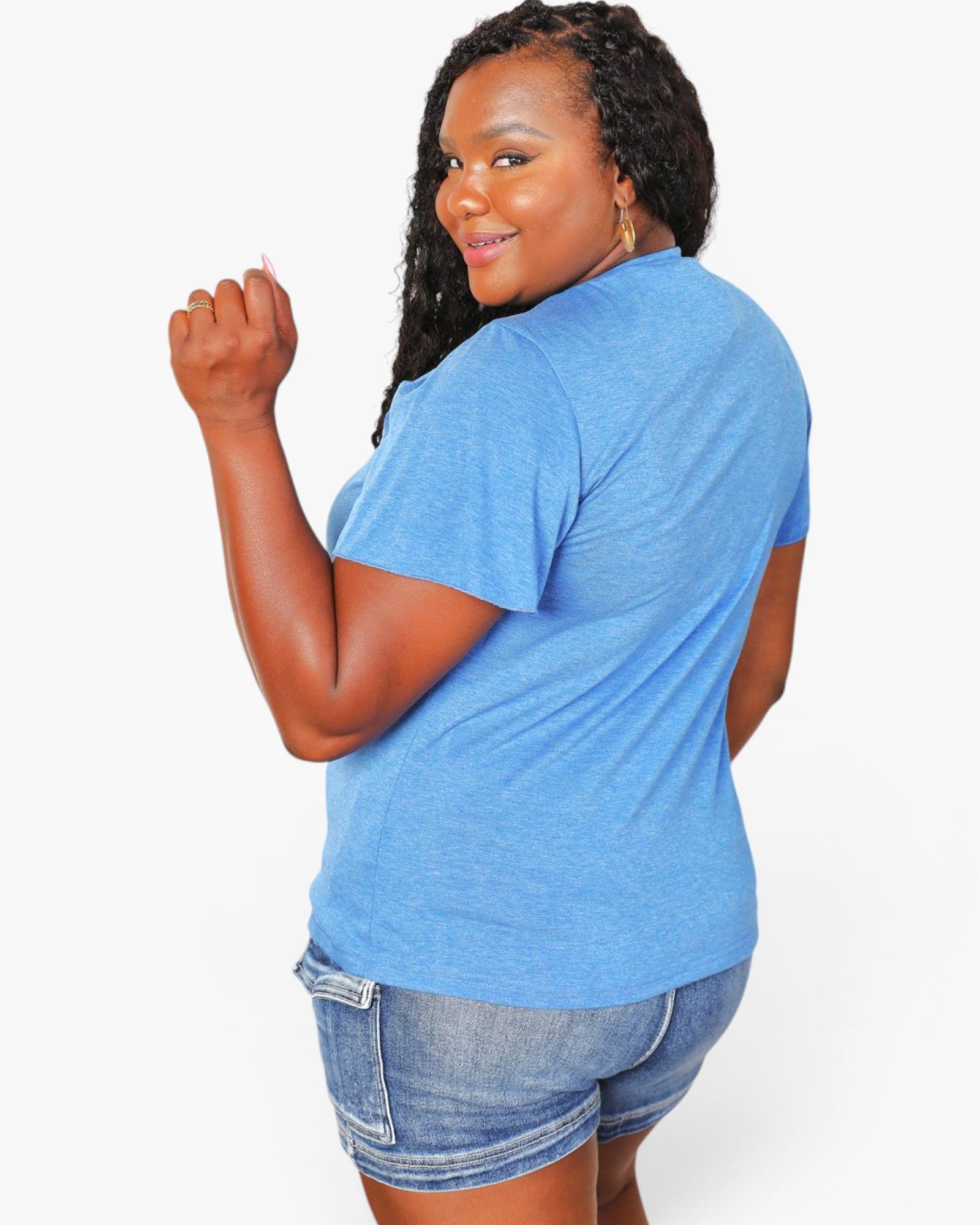 A woman wearing a heather blue short-sleeve t-shirt and denim shorts, shown from a back-three-quarter angle against a plain white studio background.
