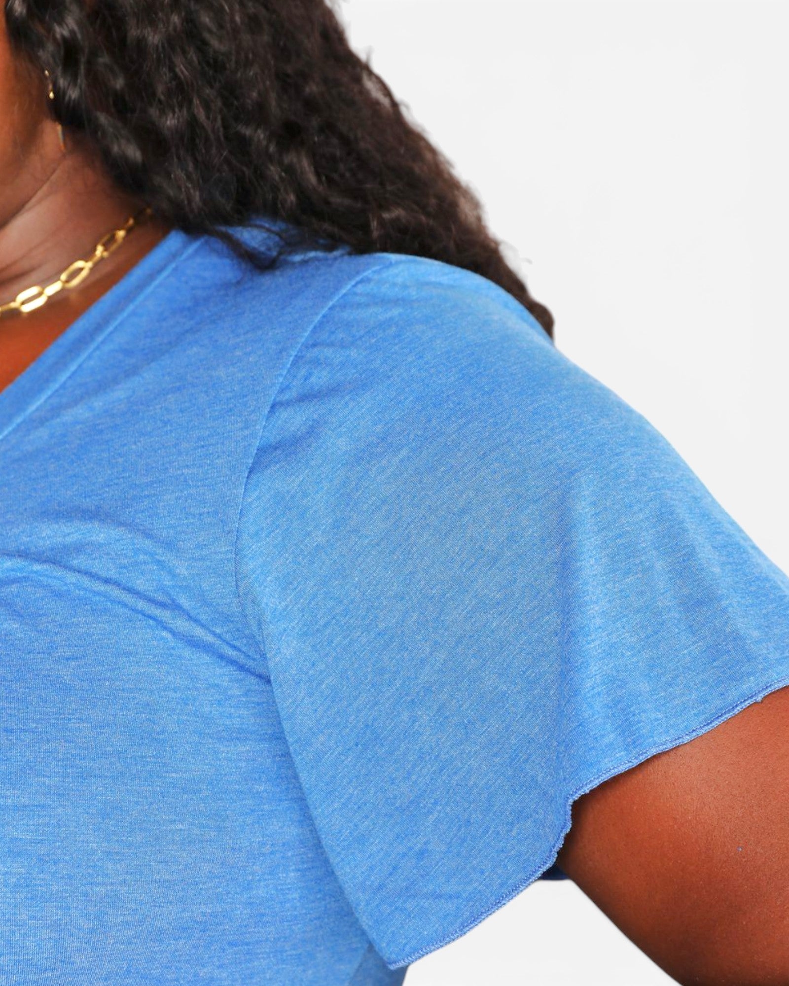 Close-up of a person wearing a heathered blue short-sleeve V-neck T-shirt, showing the shoulder, collarbone, and part of the hair and skin against a plain light background.