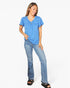 A woman modeling a heather blue short-sleeve V-neck top with a gathered chest detail and light-wash blue jeans, standing against a plain white studio background.