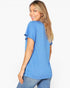 A woman with blonde-highlighted hair is shown from a back-three-quarter angle wearing a heathered blue short-sleeve top with ruffle details on the sleeves and blue jeans against a plain white background.