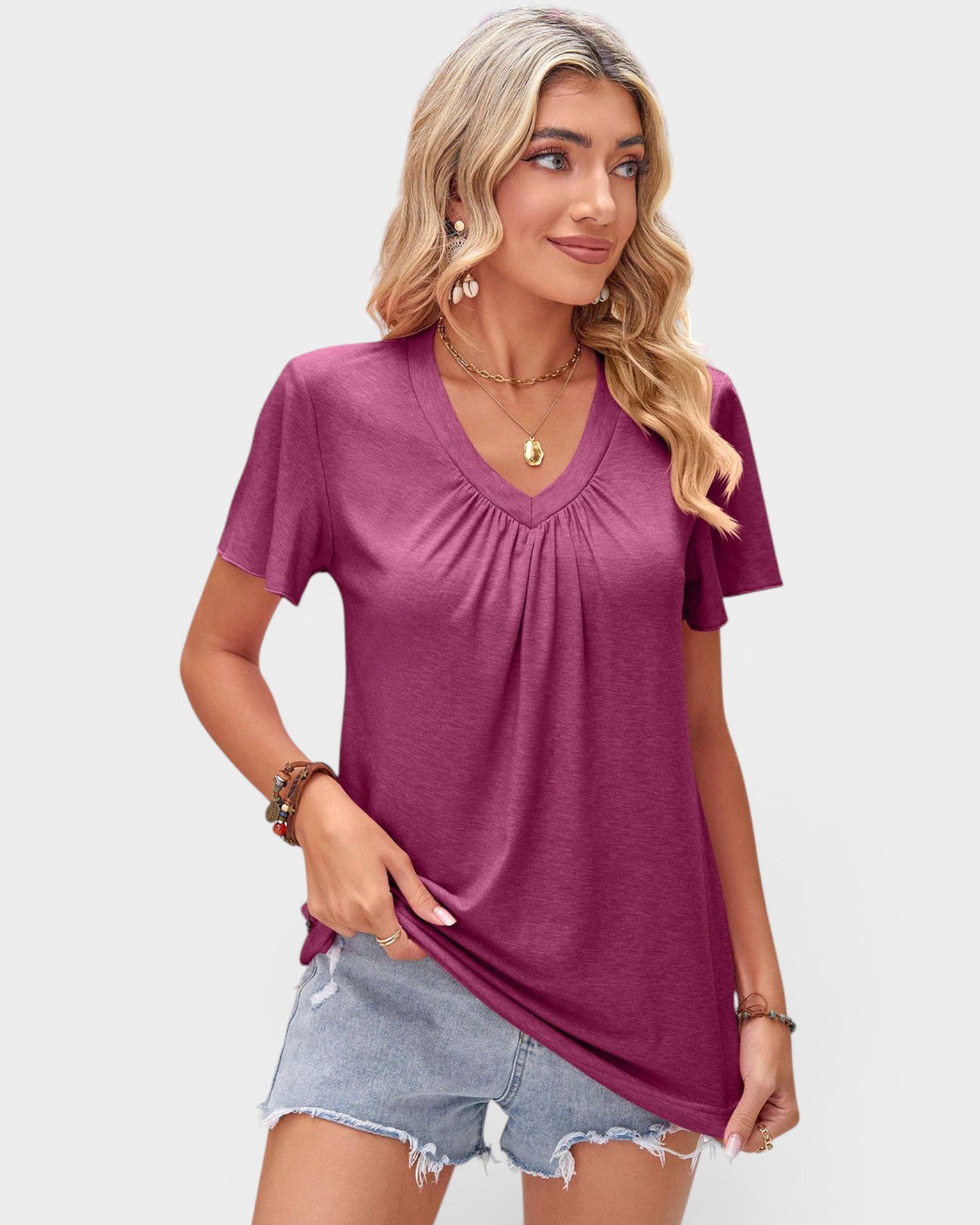 Woman wearing a magenta top and denim shorts on a plain background