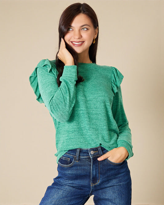 Woman wearing a green sweater with ruffled sleeves and blue jeans on a beige background