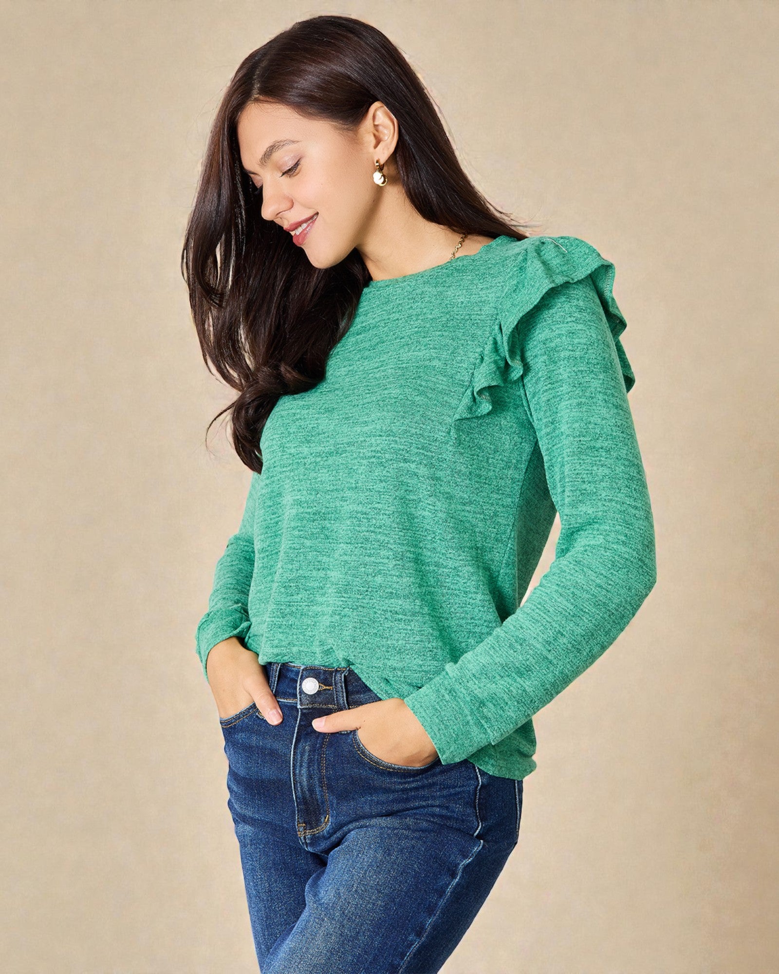 Woman wearing a green sweater with ruffled shoulders against a beige background