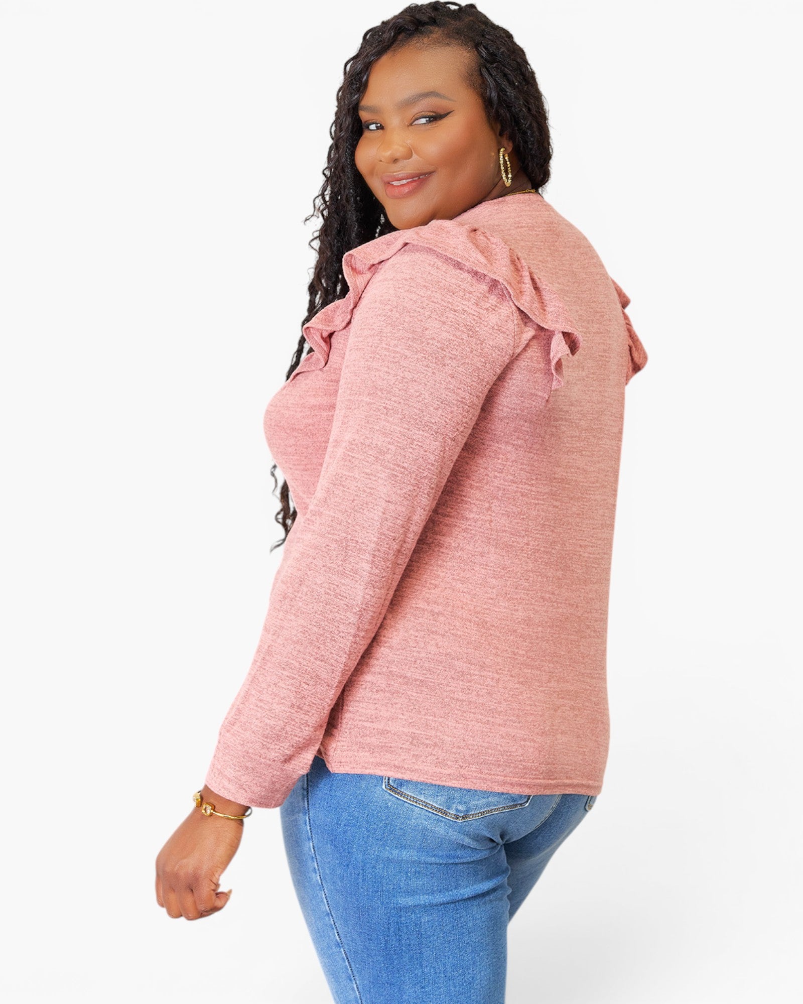 A woman wearing a heathered pink long-sleeve top with ruffled shoulder details, paired with blue jeans, photographed against a clean white background.
