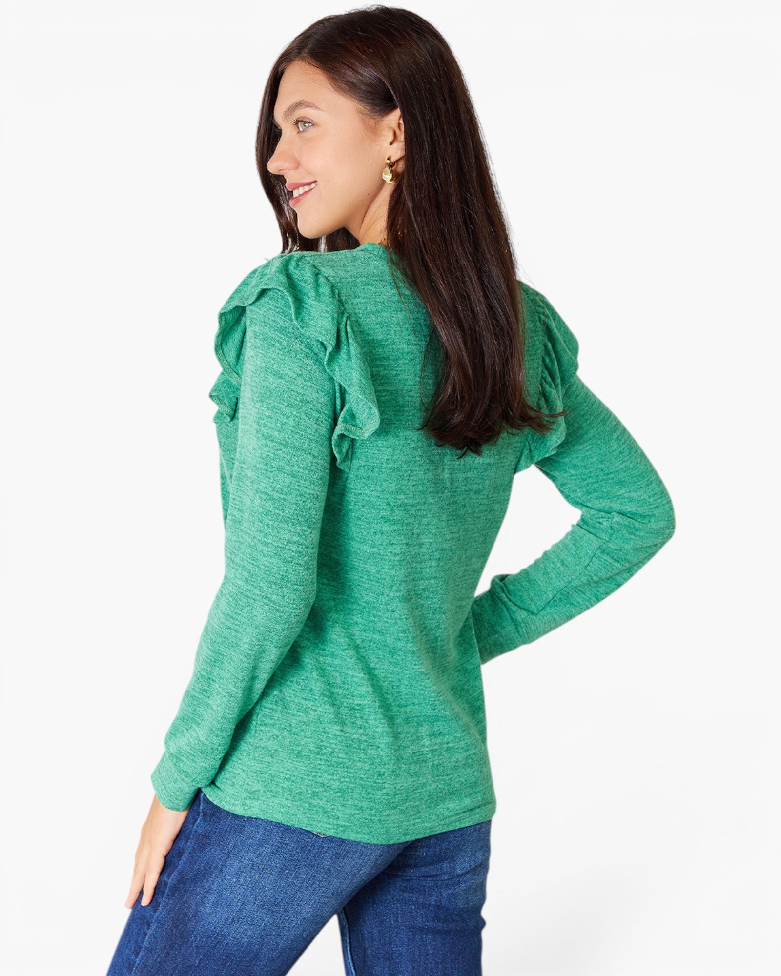 A woman wearing a green long-sleeve knit top with ruffled shoulder details, shown from a side-back angle against a plain white studio background.