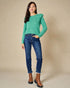 Woman wearing a green sweater with ruffled sleeves and blue jeans on a beige background