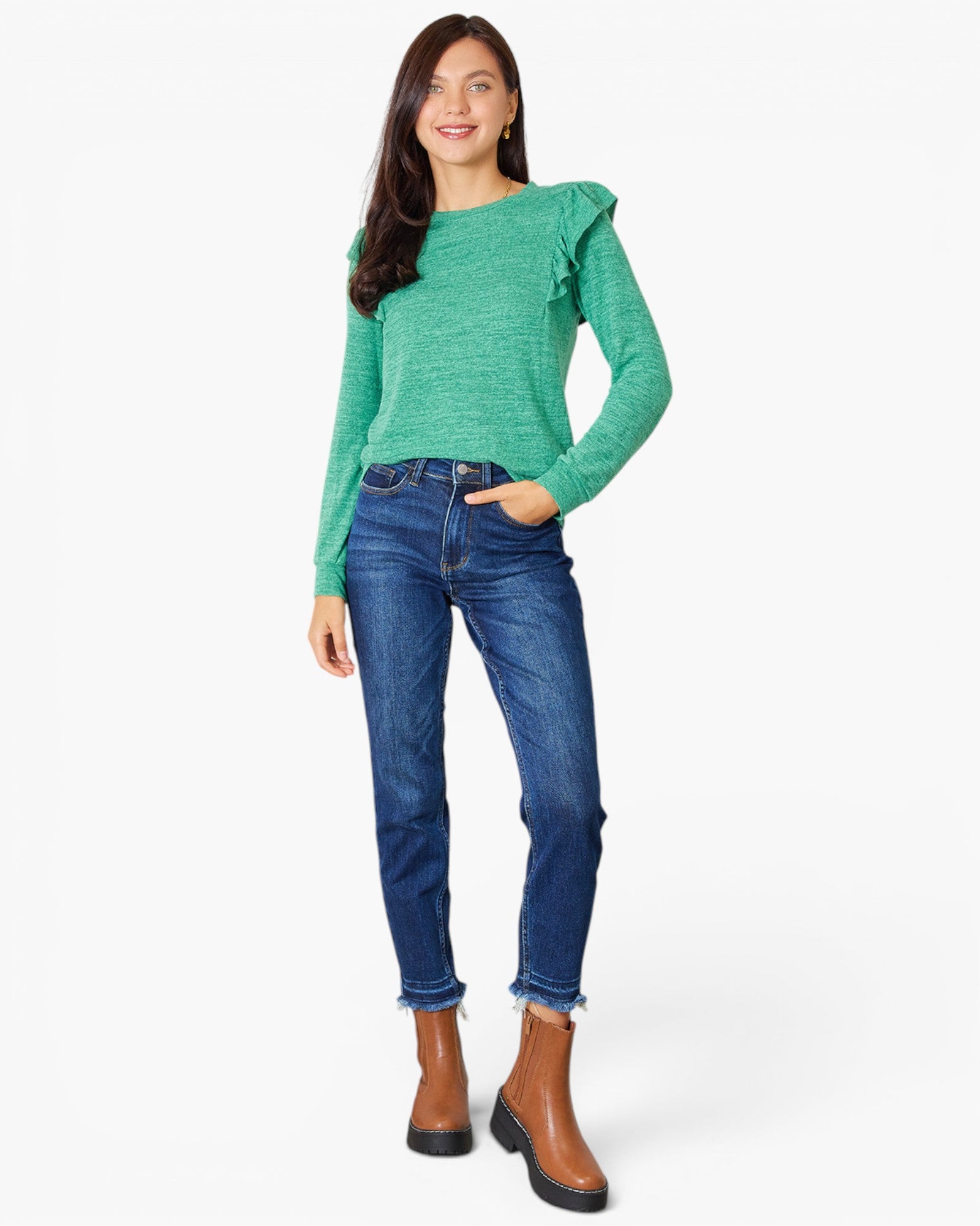 A woman modeling a green long-sleeve knit top with ruffled shoulder details, paired with blue jeans and brown ankle boots, against a plain white studio background.