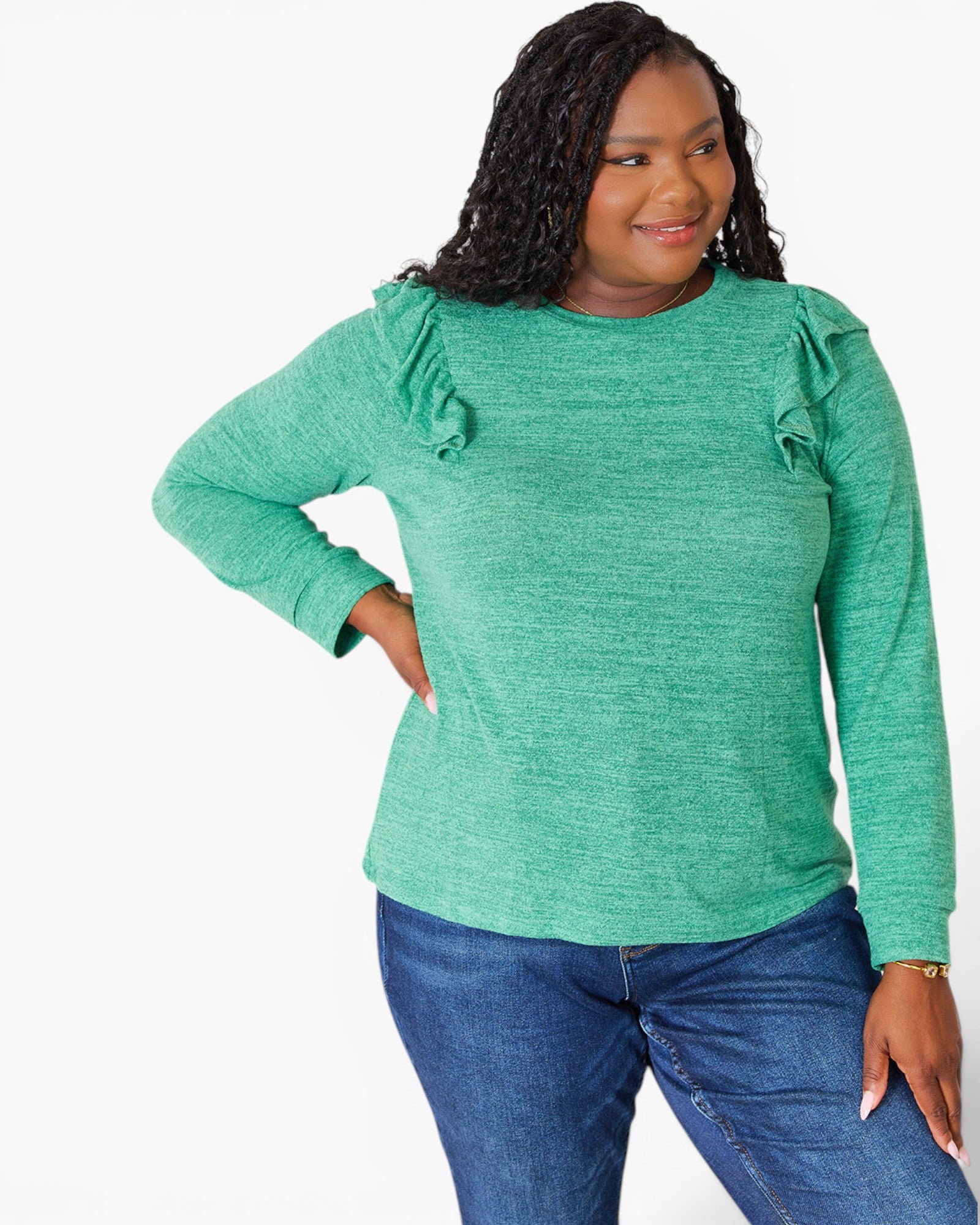 A woman modeling a heather green long-sleeve top with ruffle details on the shoulders, paired with blue jeans, against a plain white background.