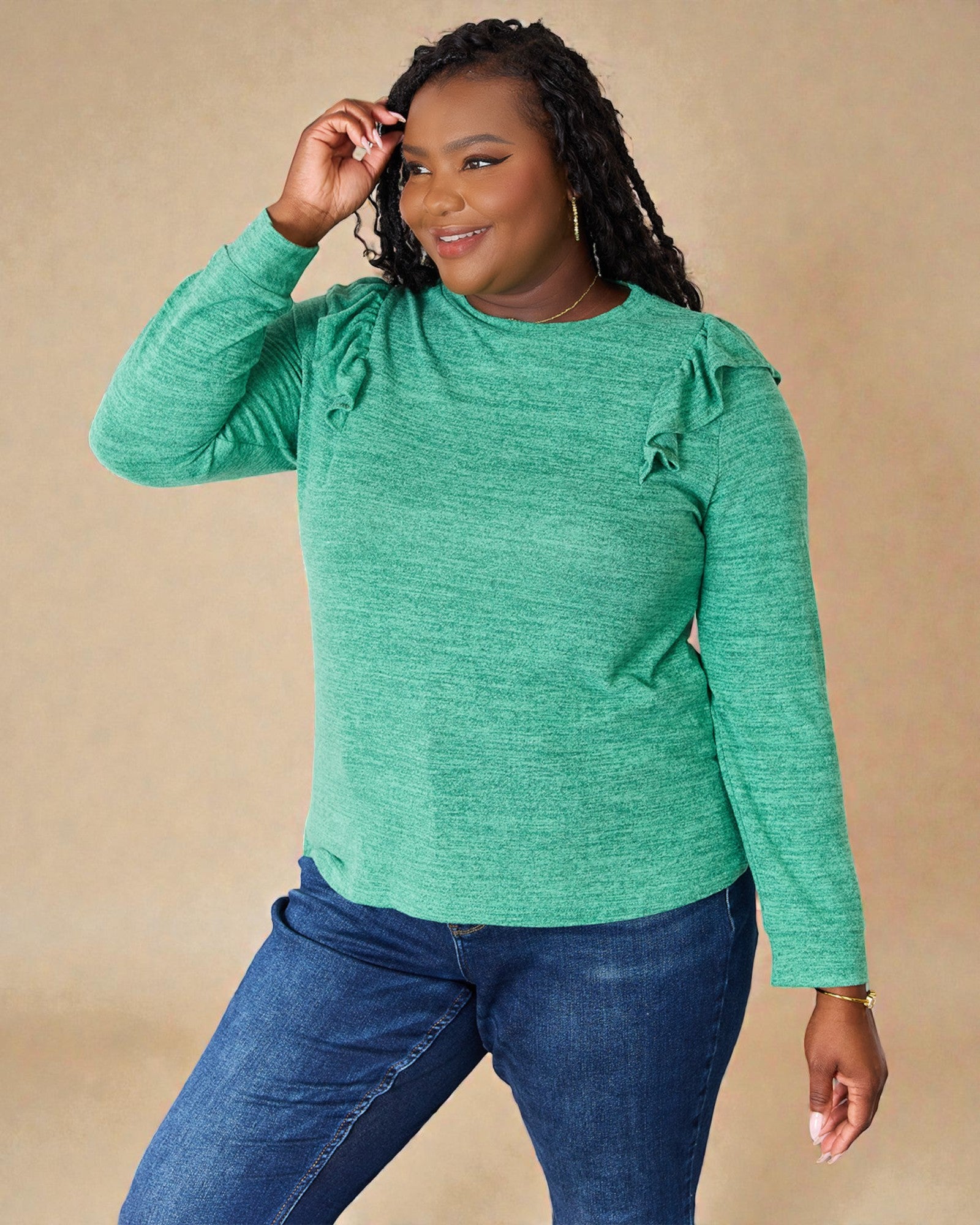 Woman wearing a green long-sleeve top with ruffled shoulders against a beige background