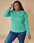 Woman wearing a green long-sleeve top with ruffled shoulders against a beige background