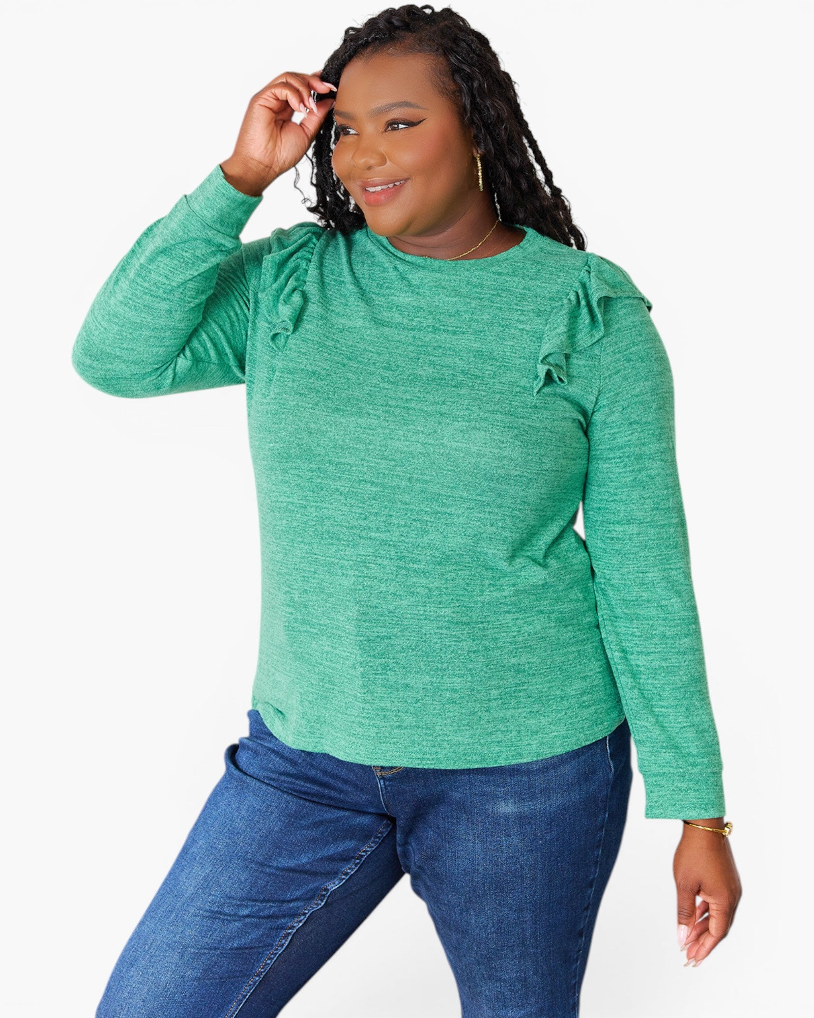 A woman modeling a green long-sleeve top with ruffle details on the shoulders, paired with blue jeans, against a plain white background.