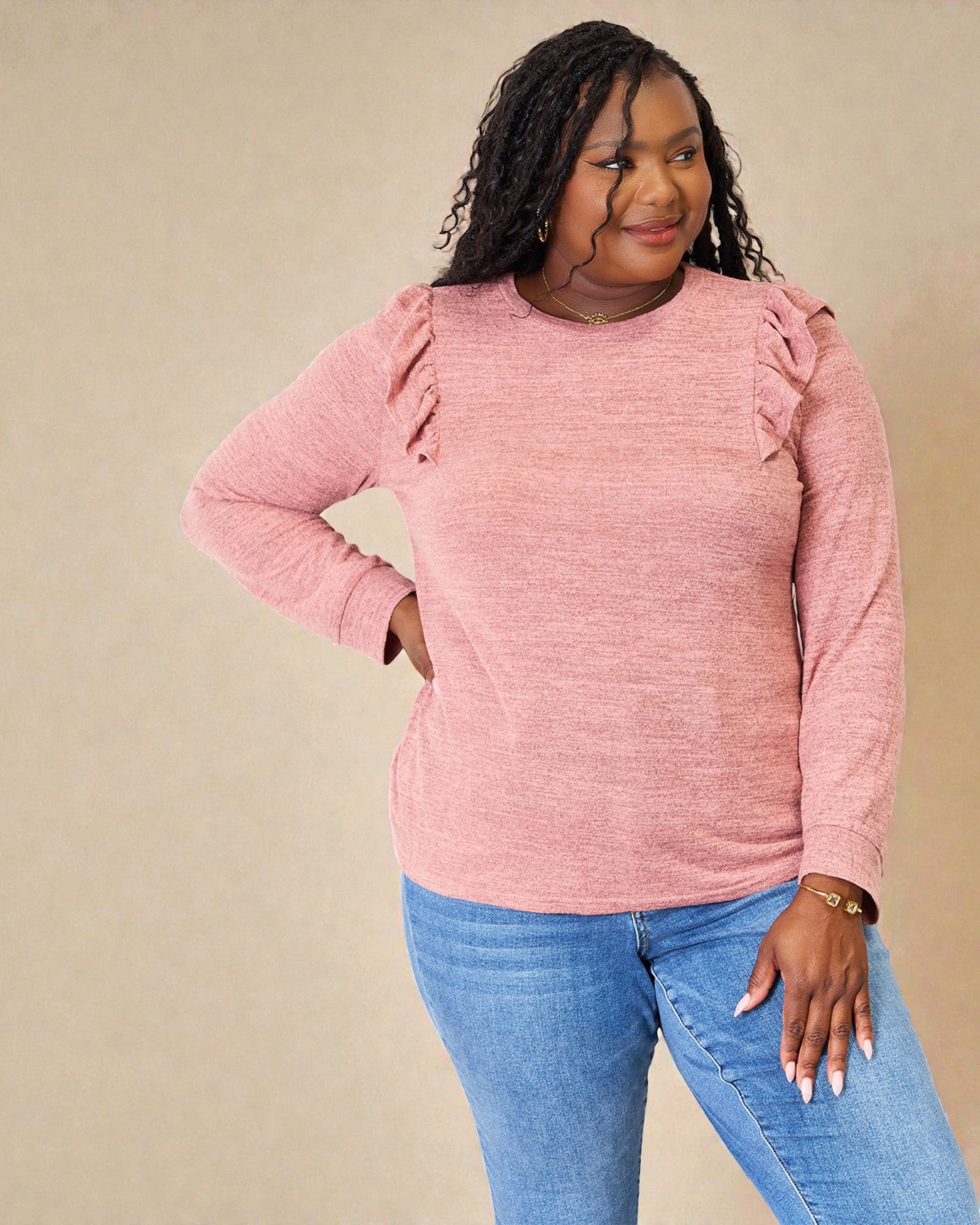 Woman wearing a pink sweater with ruffled shoulders against a beige background