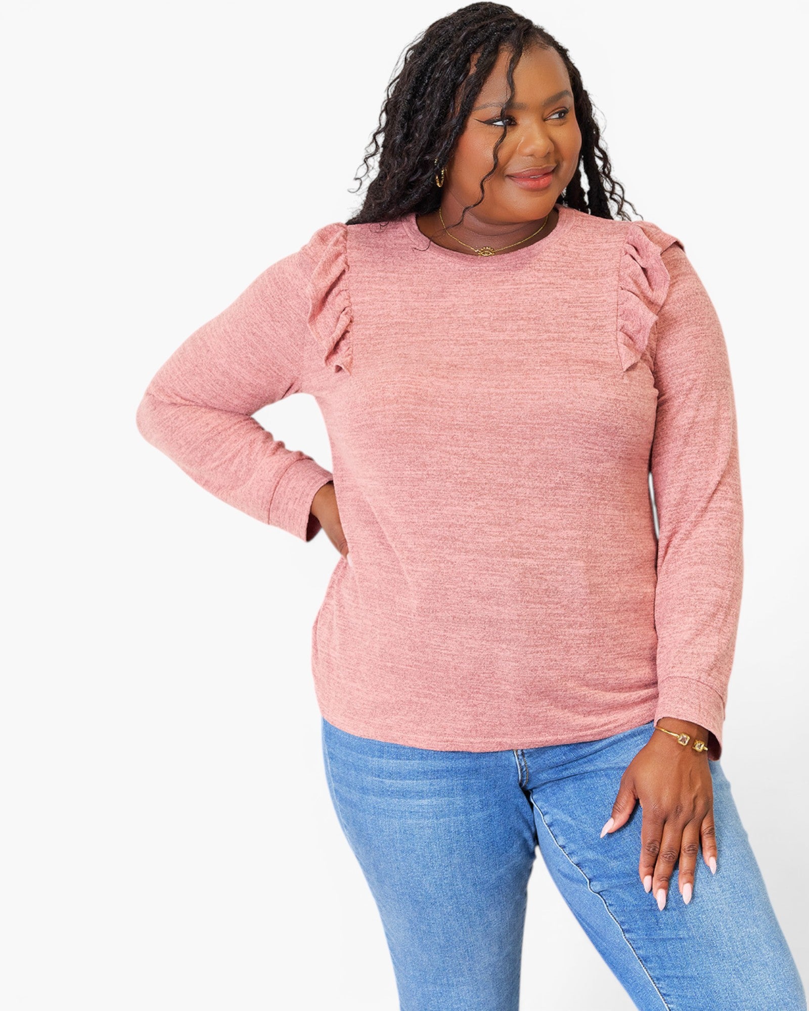 A woman modeling a heathered pink long-sleeve top with ruffle details on the shoulders, paired with blue jeans, against a plain white background.