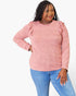 A woman modeling a heathered pink long-sleeve top with ruffle details on the shoulders, paired with blue jeans, against a plain white background.