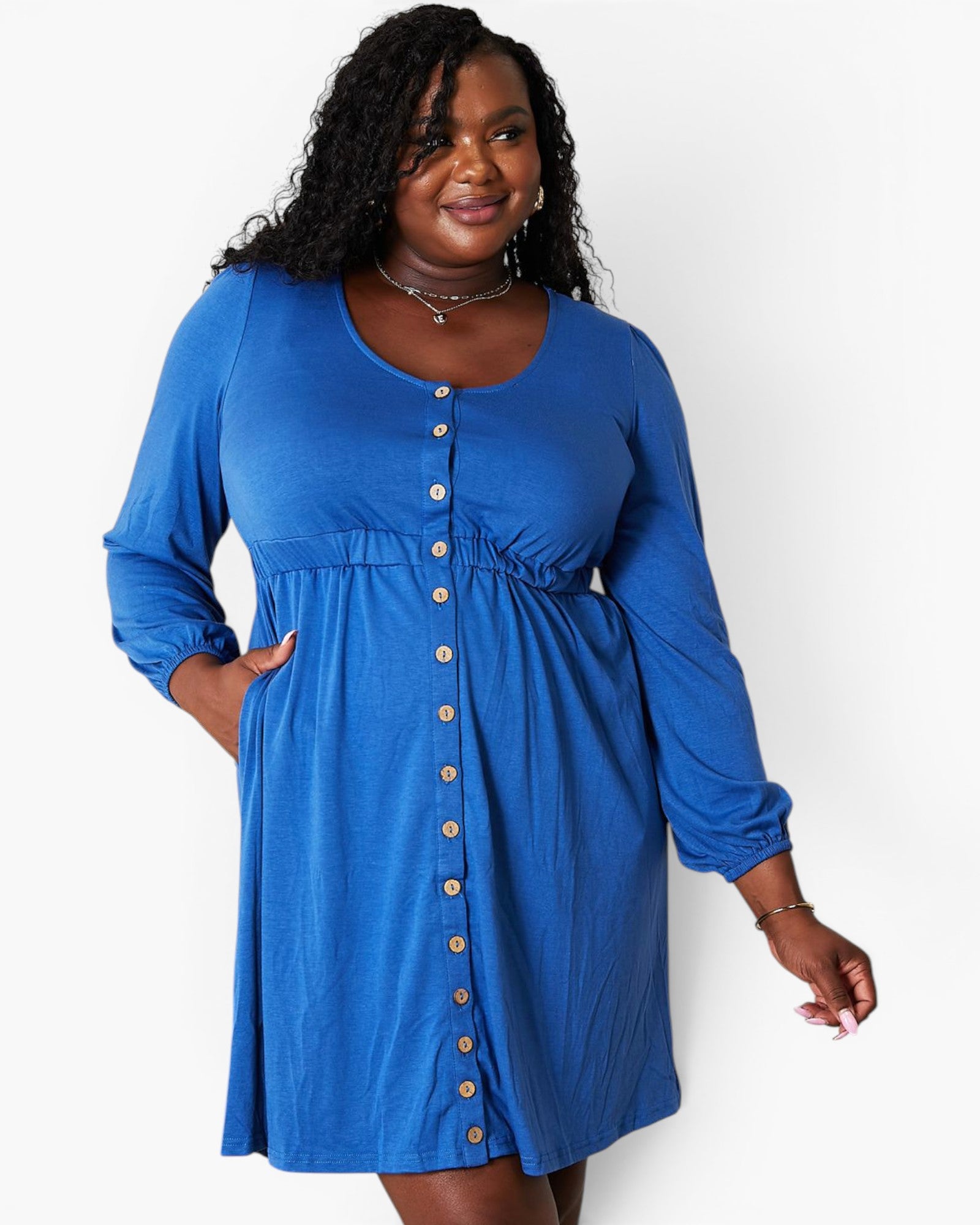 A woman modeling a bright blue long-sleeve maternity dress with a button-down front and gathered waist, set against a plain white studio background.