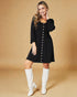 Woman wearing a black dress with white buttons and white knee-high boots on a beige background