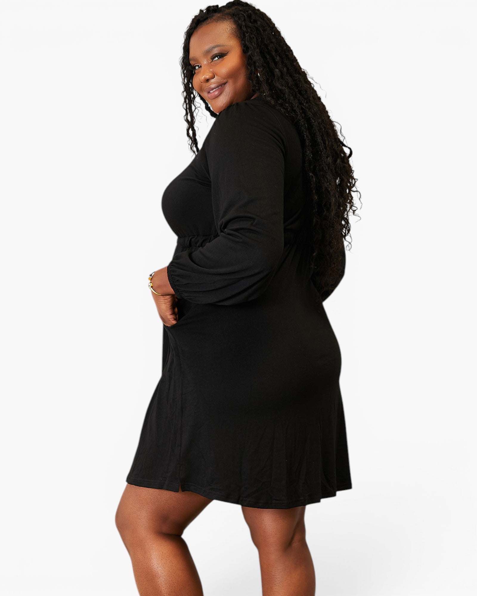 A woman modeling a black long-sleeve mini dress, shown from a side-back angle against a plain white studio background.