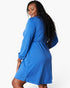 A woman modeling a bright blue long-sleeve dress with a gathered waist, shown from a three-quarter back angle against a plain white studio background.