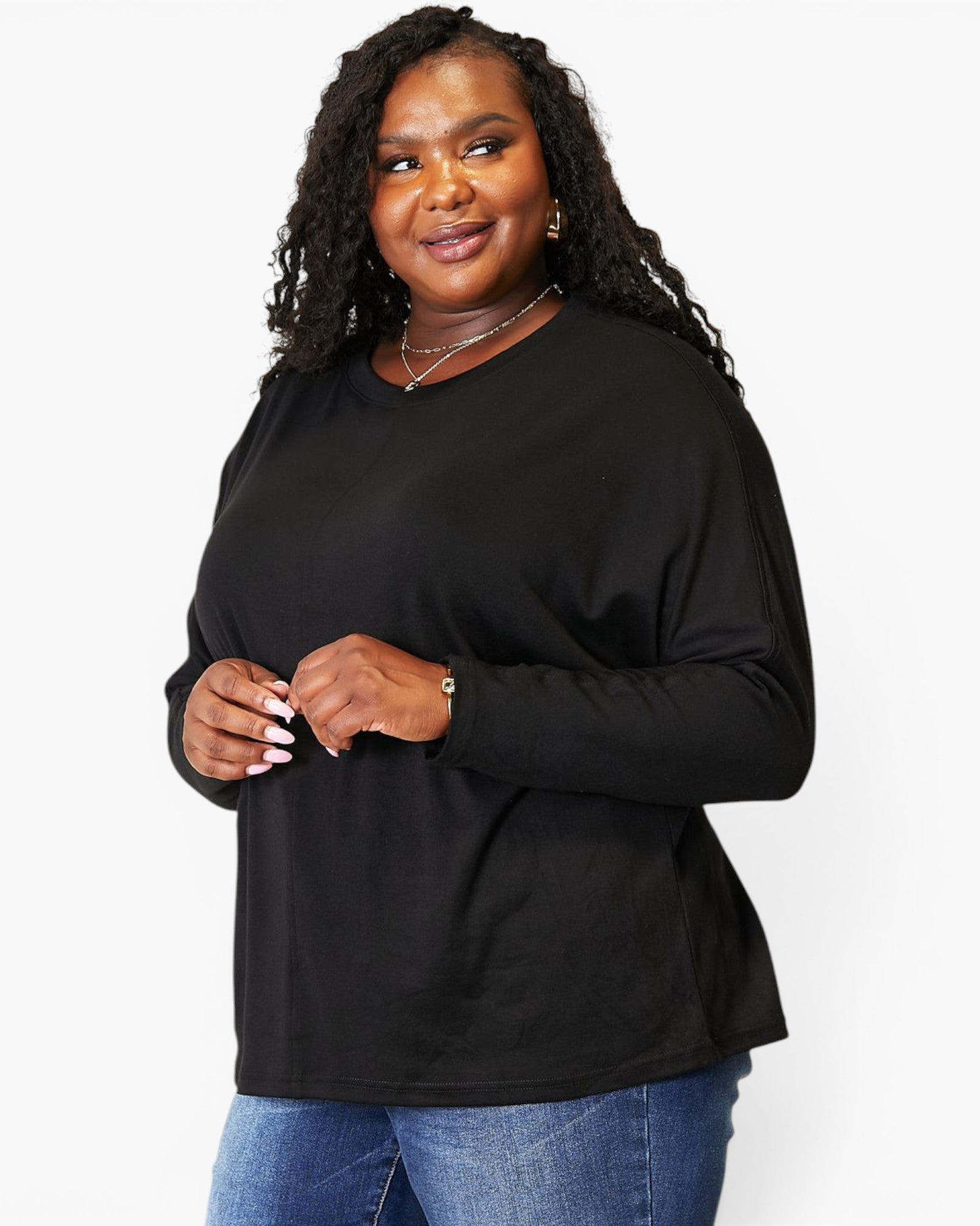A woman modeling a black long-sleeve crewneck top with a relaxed fit, paired with blue jeans, against a plain white studio background.