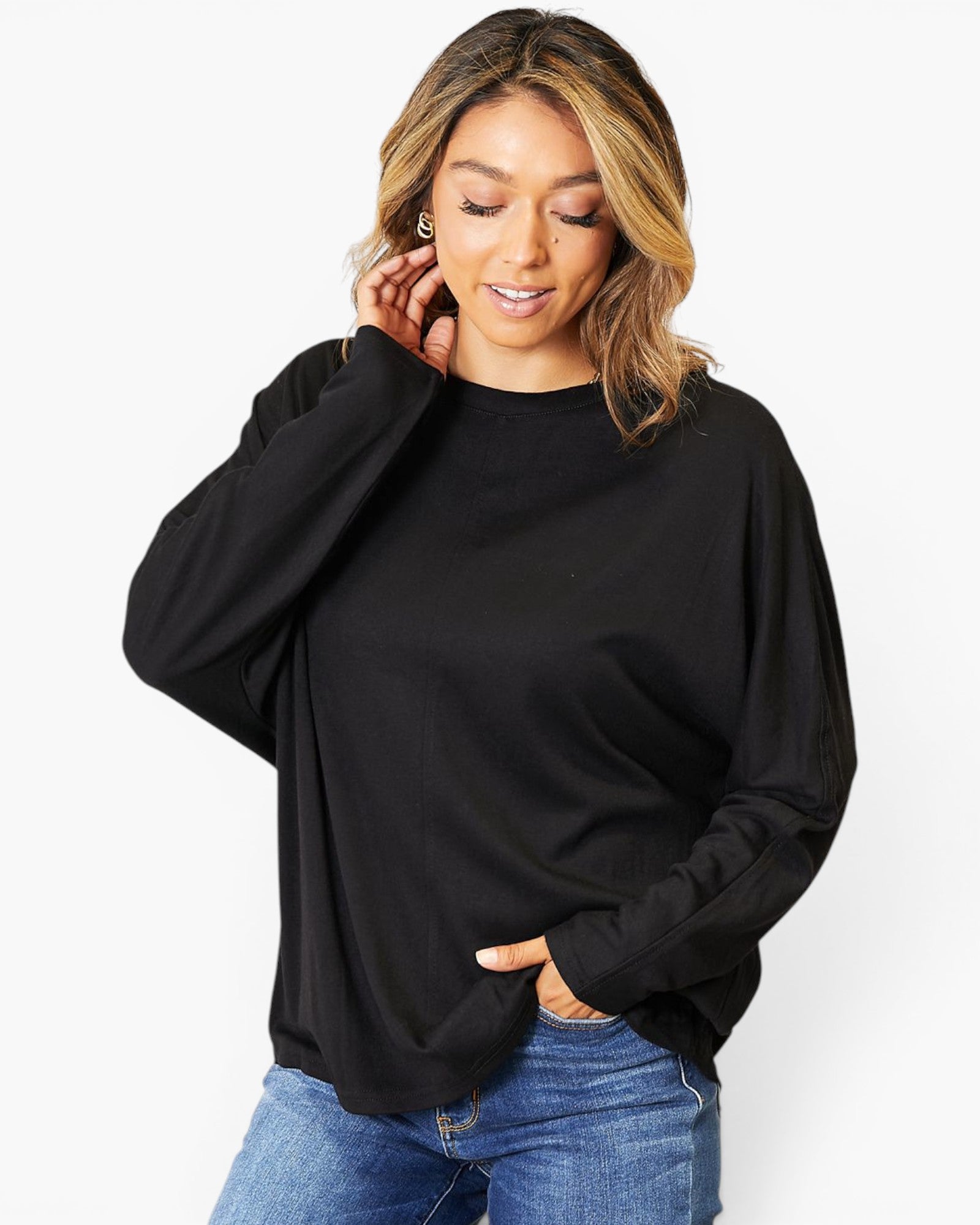 A woman wearing a black long-sleeve crewneck top and blue jeans, posing against a plain white background.