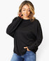 A woman wearing a black long-sleeve crewneck top and blue jeans, posing against a plain white background.