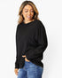 A woman wearing a black long-sleeve top and blue jeans, standing against a plain white studio background.