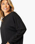 A woman wearing a black long-sleeve top, shown from the chest up against a plain white background.