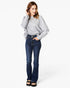 A woman modeling a light gray long-sleeve top and dark blue flared jeans with black sandals, standing against a plain white studio background.