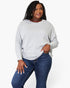 A woman modeling a light gray long-sleeve knit top with a relaxed fit, paired with dark blue jeans, against a plain white studio background.