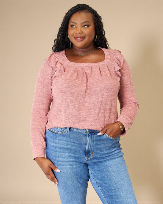 Woman wearing a pink blouse and blue jeans against a beige background