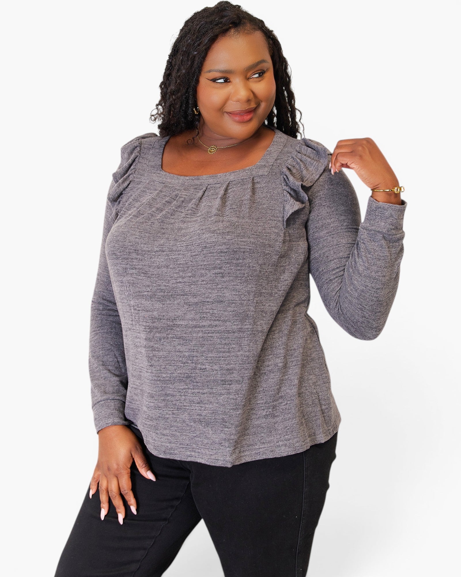 A woman modeling a heather gray long-sleeve top with ruffled shoulder details, paired with black pants, against a plain white background.