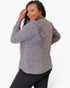 A woman modeling a heather gray long-sleeve top from the back, featuring ruffled shoulder details and a relaxed fit, paired with black pants against a plain white background.