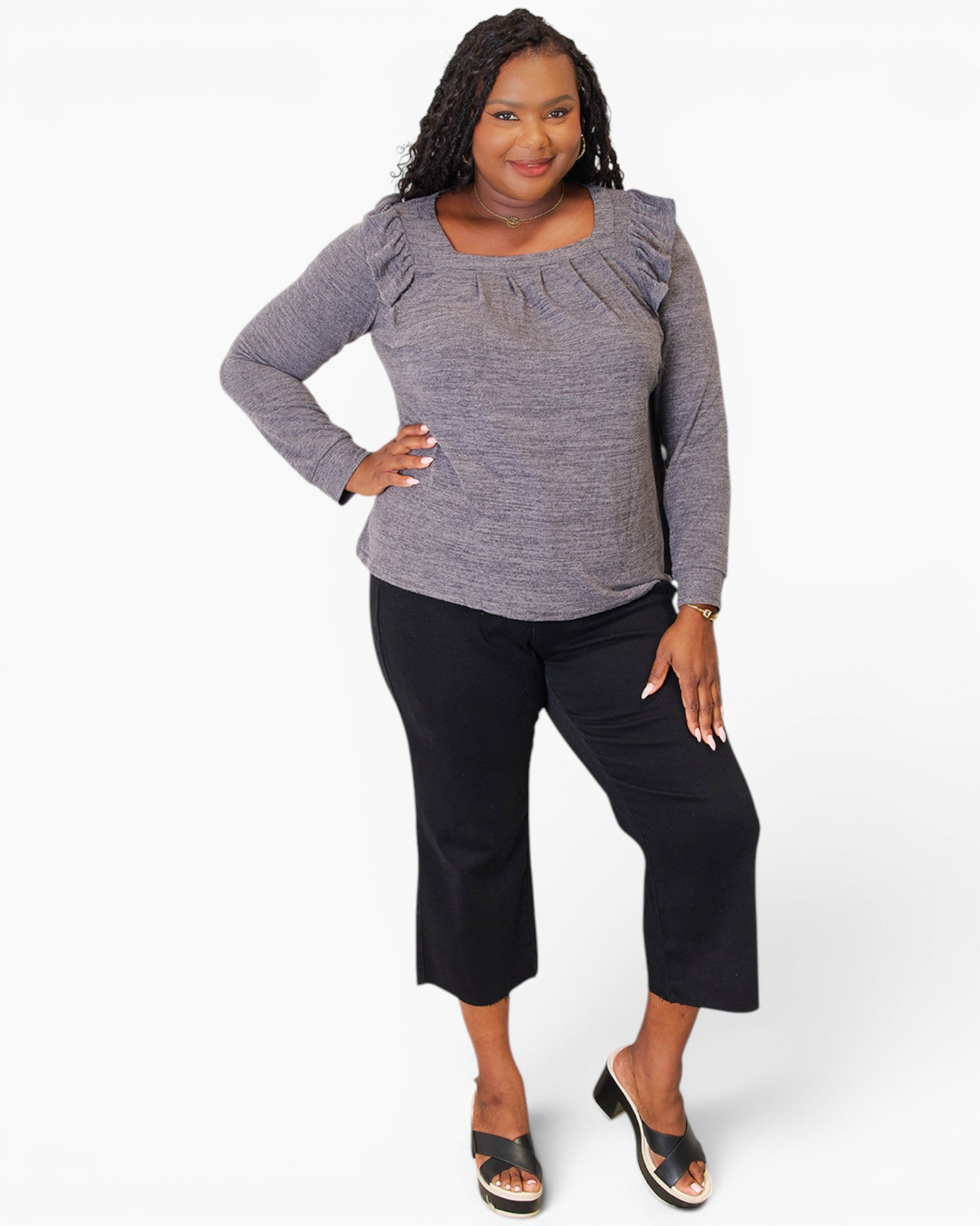 A woman modeling a heather gray long-sleeve top with ruffled shoulders and black cropped pants, standing against a plain white studio background.