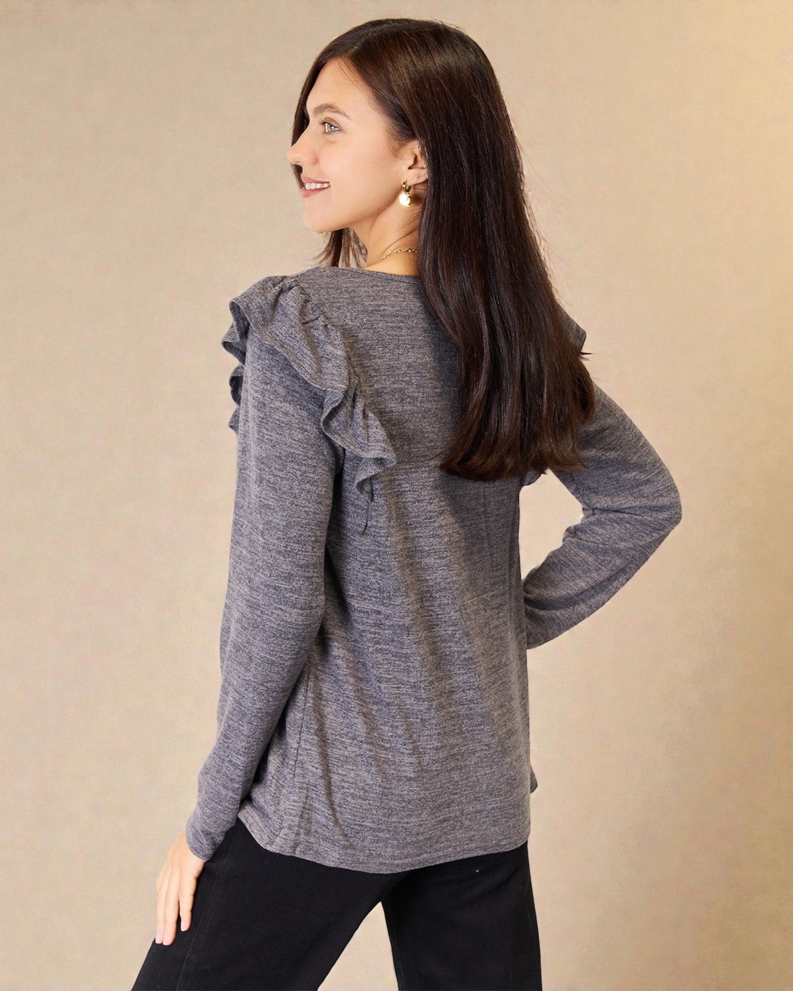 Woman wearing a gray ruffled long-sleeve top against a beige background