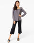 A woman modeling a gray long-sleeve top with ruffled shoulder details and black cropped pants, standing against a plain white studio background.