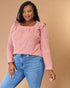 Woman wearing a pink blouse with ruffled shoulders and blue jeans on a beige background