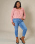 Woman wearing a pink top and blue jeans with brown boots against a beige background
