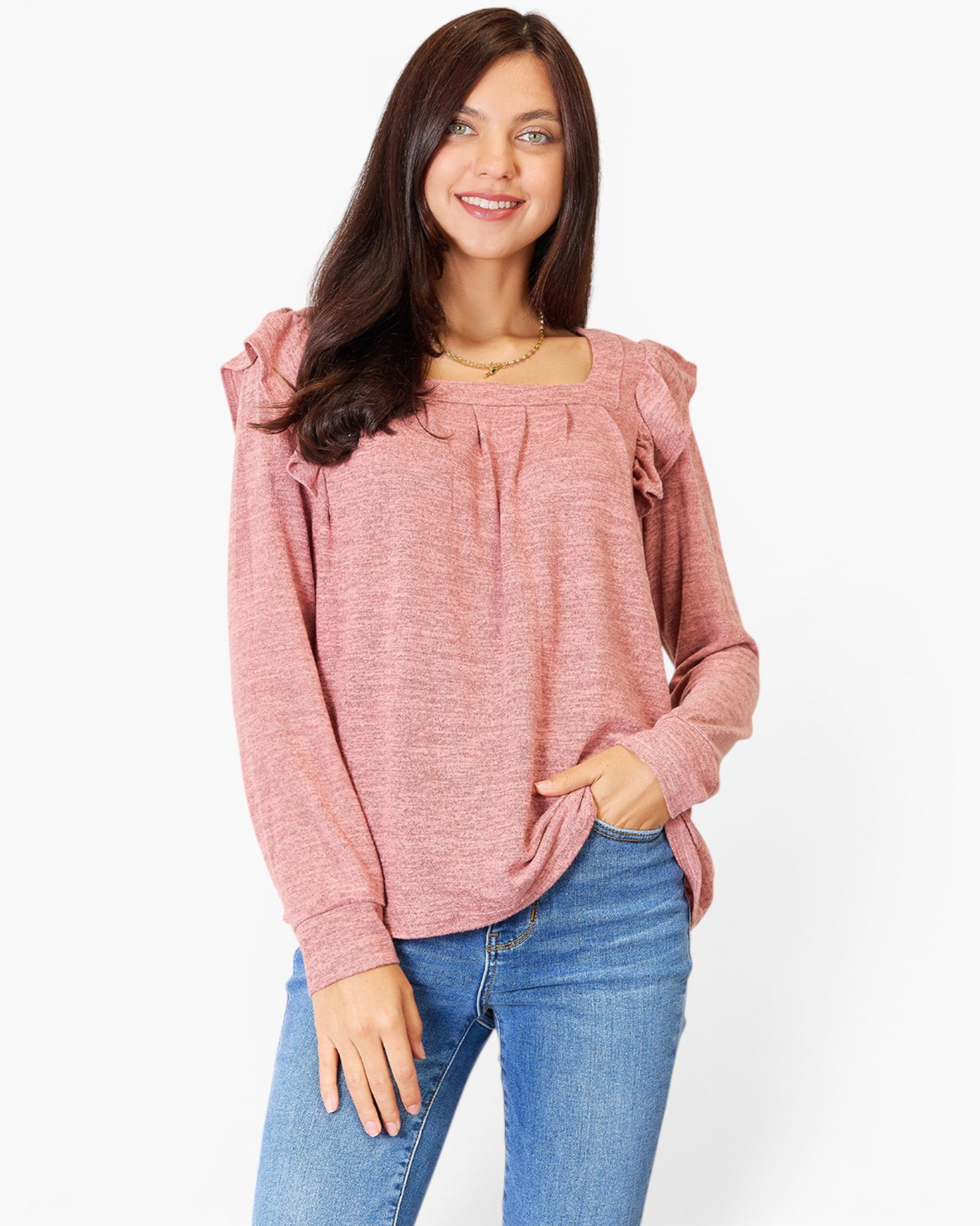 A woman wearing a dusty rose long-sleeve top with ruffled shoulder details and a gathered neckline, paired with blue jeans, against a plain white background.