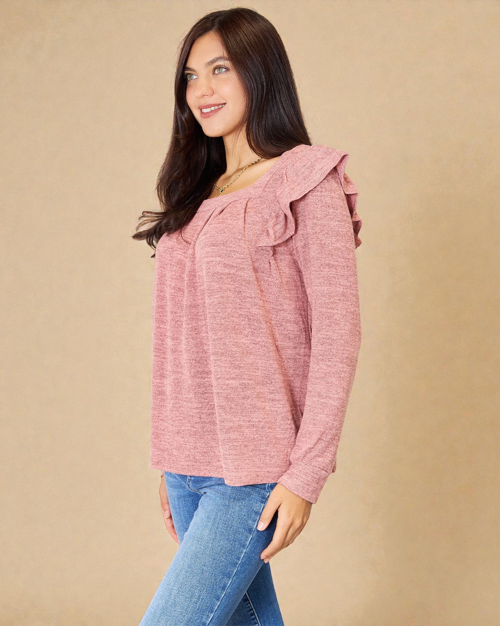 Woman wearing a pink ruffled top and blue jeans against a beige background
