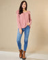 Woman wearing a pink sweater, blue jeans, and brown boots on a beige background