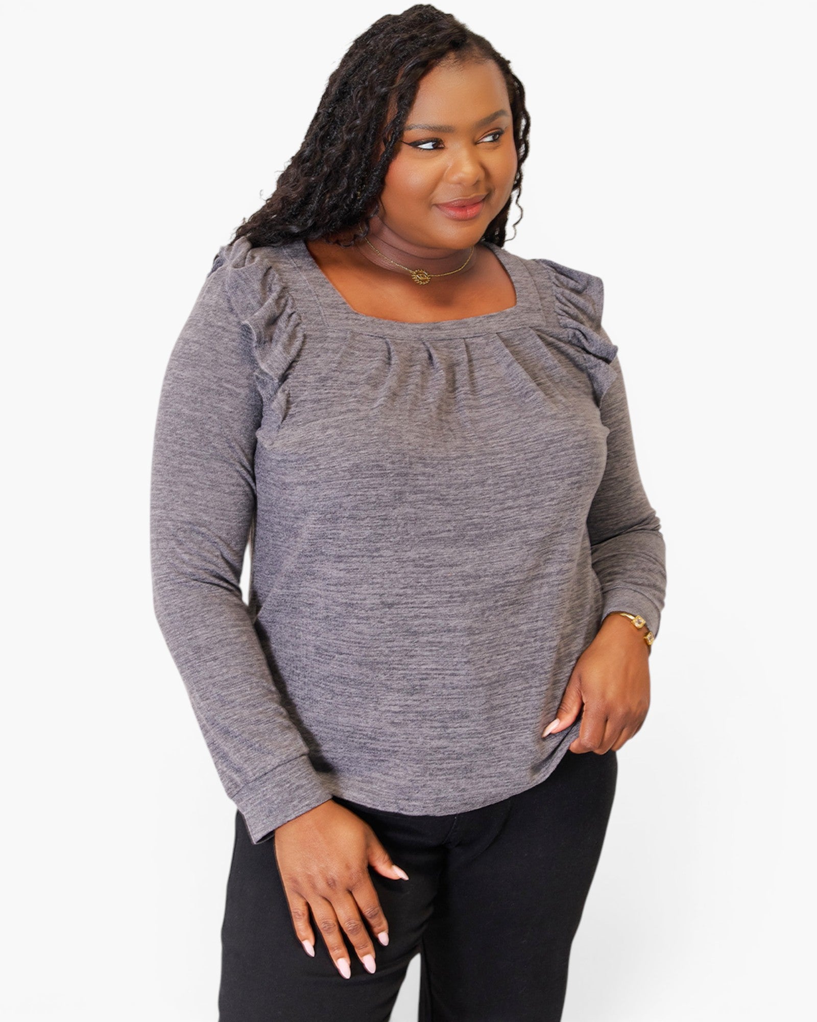 A woman wearing a heather gray long-sleeve top with ruffled shoulder details and a square neckline, paired with black pants, against a plain white background.
