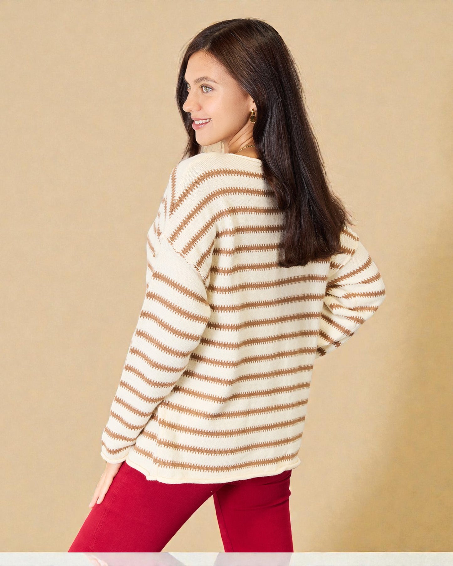Woman wearing a striped sweater and red pants against a beige background