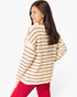 A woman wearing a cream and brown horizontally striped knit sweater, shown from a side-back angle against a plain white studio background.