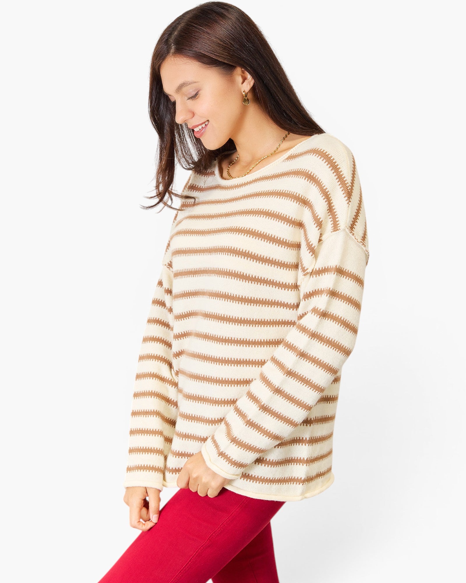 A woman wearing a cream and tan striped knit sweater and bright pink pants, shown from the waist up against a plain light gray studio background.