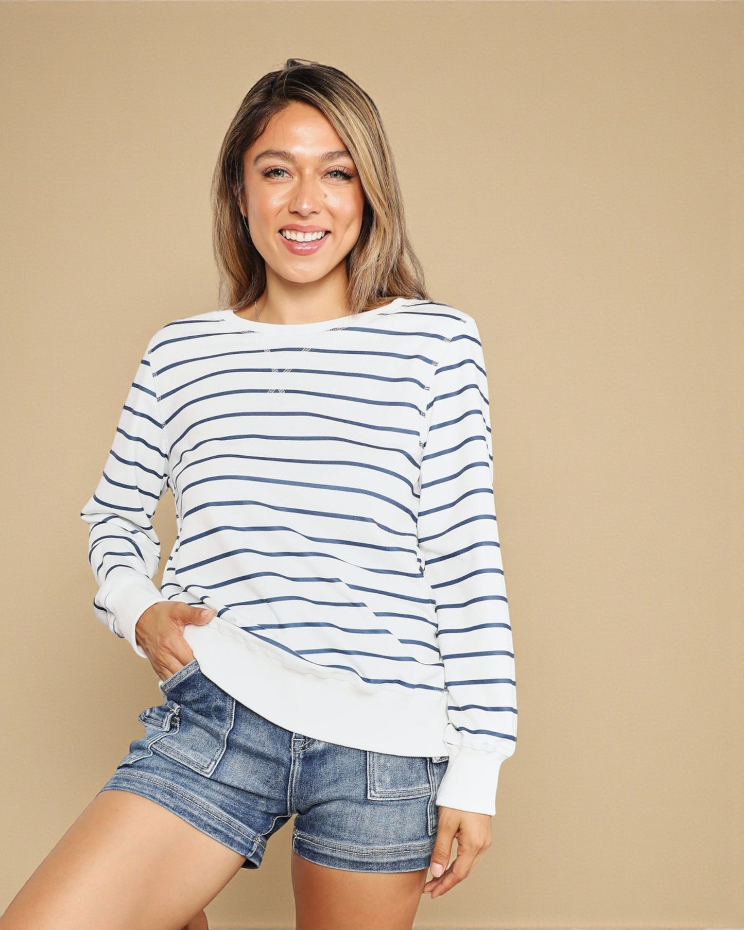 Woman wearing a striped sweater and denim shorts on a beige background