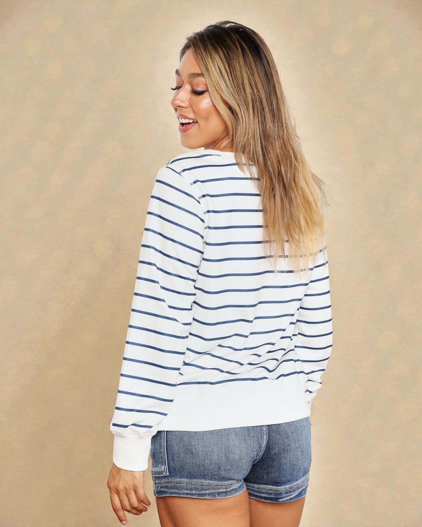 Woman wearing a striped long-sleeve shirt and denim shorts on a beige background